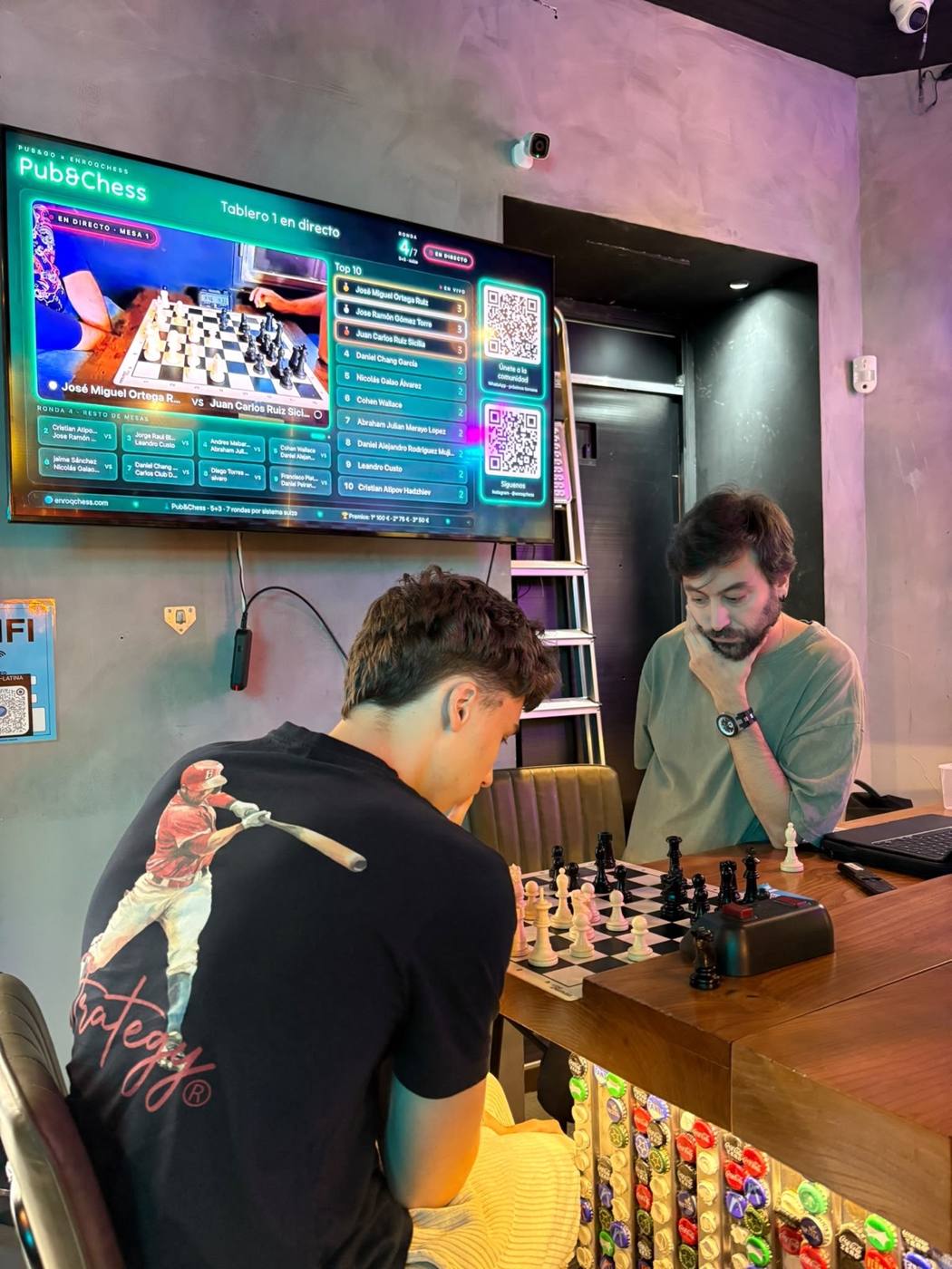 Dos jugadores jóvenes con la tele del torneo al fondo
